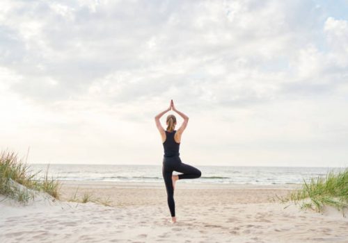 A young woman wearing gym clothes doing yoga on the beach on a sunny day.